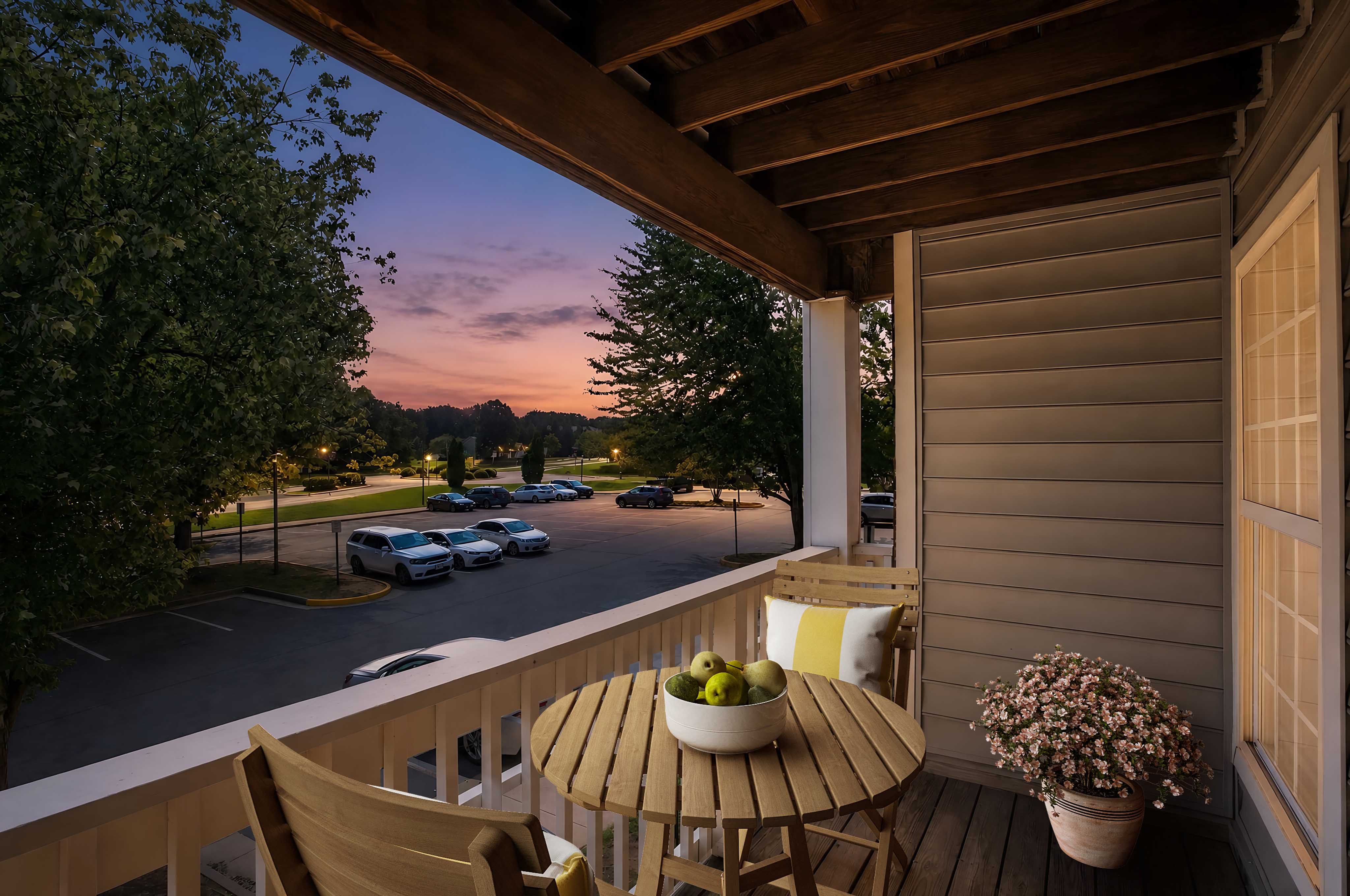 A wooden table with a bowl of fruit on it sits on a porch.